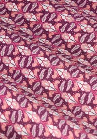 Stoff mit einem detaillierten, sich wiederholenden Blumenmuster in Pink, Weiß und Grün auf einem burgunderroten Hintergrund, der Falten und Textur zeigt.