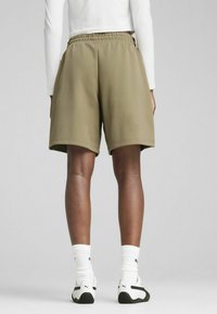Pantalones cortos deportivos color caqui con cintura elástica, corte suelto y tejido texturizado. Combinados con calcetines blancos y zapatillas en blanco y negro.
