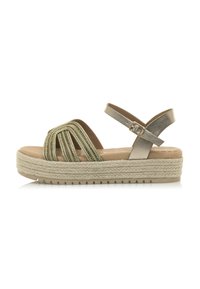 Espadrille-sandaali, jossa on vihreät punotut hihnat, metalliset yksityiskohdat ja luonnollinen juuttikoroke. Solkikiinnitys nilkkahihnassa.