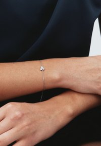 Braccialetto d'argento con tre piccole pietre chiare, con un design a catena delicata, indossato su un polso contro uno sfondo scuro.