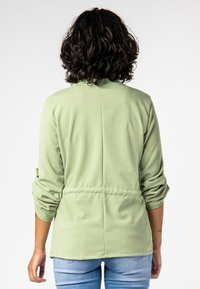 Groene lichtgewicht jas met een gladde textuur, voorzien van een tailleband, lange mouwen en een relaxte pasvorm. De achterkant heeft een naaddetail.