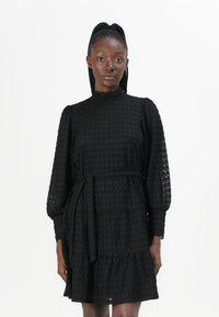 Abito nero realizzato in tessuto testurizzato, con colletto alto, lunghe maniche a sbuffo, design a balze e una cintura in vita per una vestibilità regolabile.