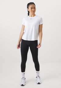 Valge lühikeste varrukatega sportlik T-särk, millel on must Nike'i logo. Ühildub mustade retuuside ja valgete tossudega, millel on mustad detailid.