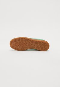 Nike sportbačiai su tekstūruota ruda guma pado dalimi, hexagonaliniu raštu, žalia viršutine dalimi ir minimalizmu.