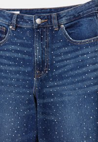 Jeans in denim con un lavaggio blu scuro, decorati con strass sparsi, tasche frontali funzionali e chiusura con bottone in metallo.
