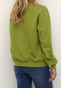 Sudadera verde con cuello redondo, puños acanalados y dobladillo elástico, combinada con jeans azules. El material parece suave y ligeramente texturizado.