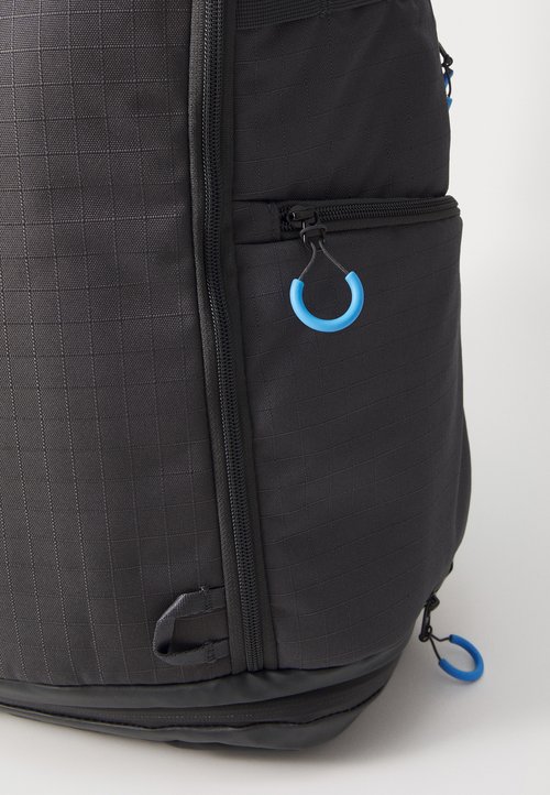 Zaino in tessuto nero con un motivo a griglia testurizzata, dotato di una tasca con zip laterale, accenti blu e una base resistente.