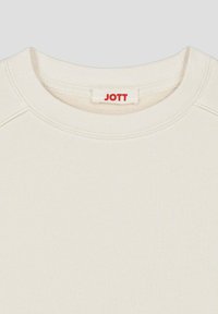 Felpa color crema con scollatura rotonda, caratterizzata da un tessuto testurizzato e un piccolo logo "JOTT" rosso al collo.