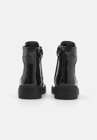 Bottines en cuir verni noir avec une finition brillante, dotées d'une fermeture éclair et d'une semelle en caoutchouc texturée. Marque Geox sur le talon.