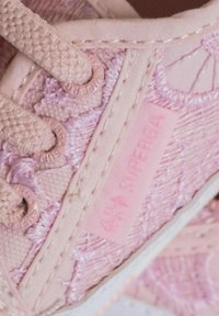 Sneaker in tela rosa con motivo floreale testurizzato, fori per i lacci tondi e etichetta con logo stampato. Presenta una suola bianca a contrasto e lacci sottili.