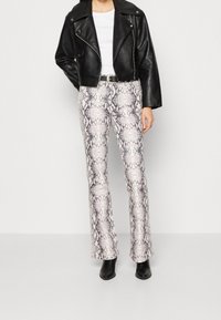 Chaqueta de motociclista de cuero negro, camiseta blanca y pantalones acampanados de estampado de serpiente con una textura brillante. Botines negros completan el conjunto.