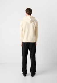 Felpa crema con cappuccio regolabile, abbinata a pantaloni larghi neri. Il tessuto appare morbido e liscio, senza motivi visibili.