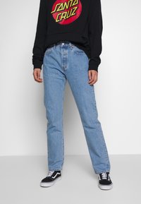 Jeans de ganga azul claro com corte straight, cintura alta e uma textura desbotada. Combinados com um sweat preto e ténis pretos.