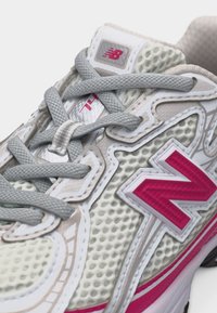 Άσπρο και μπεζ πλεκτό αθλητικό παπούτσι New Balance με γκρι κορδόνια και έντονο ροζ λογότυπο στο πλάι και στη γλώσσα.