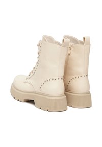 Kremowe botki sięgające kostki wykonane ze skóry, z solidną beżową podeszwą, ozdobione ćwiekami po bokach oraz zamkiem błyskawicznym z boku.