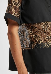 Zwarte shirt met een bloemenpatroon in kant in goud en bruin, met korte mouwen en een relaxte pasvorm. Zachte stoftextuur.