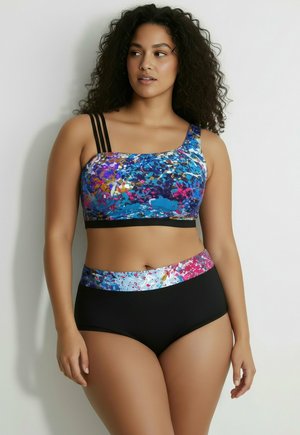 Frau trägt einen zweiteiligen Badeanzug mit multicolor abstraktem Print-Oberteil mit drei Schulterriemen und schwarzem Unterteil mit passendem Bund.