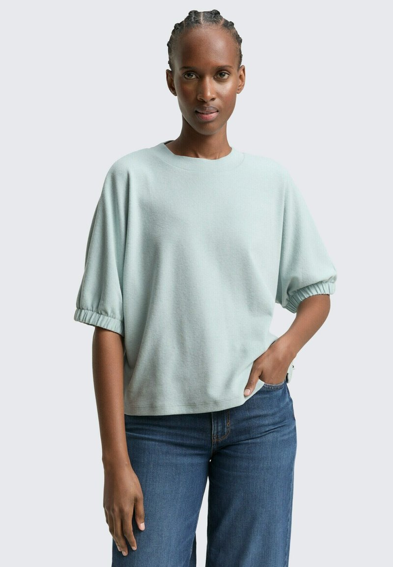 Hellgrünes, übergroßes Sweatshirt mit kurzen, elastischen Ärmeln. Weicher Stoff, runder Ausschnitt, kombiniert mit blauen Jeans.