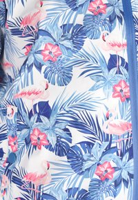 Tessuto della camicia floreale con sfondo bianco, che presenta fenicotteri rosa, fiori blu e rosa, foglie verdi e una cerniera blu di accentuazione.