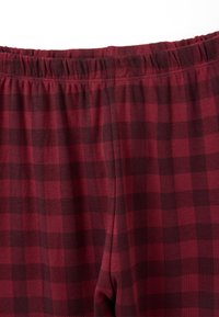 Pantalones de cuadros rojos y oscuros con una cinturilla elástica, que presentan una textura suave y un corte cuadrado. Los detalles visibles de la tela incluyen cuadros.