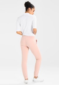 Ljust rosa joggerbyxor med elastiska muddar och midja, tillsammans med en vit t-shirt med kort ärm. Mjuk tyg med en slät textur.