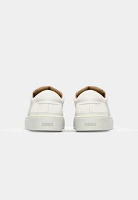 Adidași din piele albă cu o formă rotunjită, finisaj mat și un accent bej pe guler. Prezintă o talpă texturată și un logo embosat.