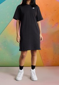 Czarna bawełniana sukienka typu t-shirt z krótkimi rękawami i prostą sylwetką. Na piersi znajduje się małe białe logo. Do kompletu białe trampki.