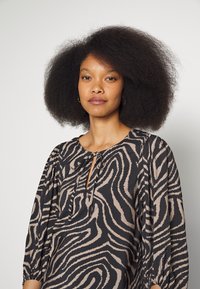 Blusa preta e bege com padrão de zebra, apresentando um decote em forma de olho-chave e mangas bufantes. Feita de um tecido leve e texturizado.