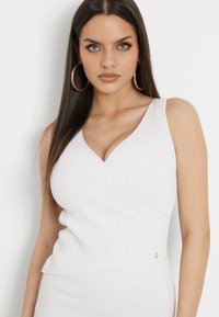 Balta šonkaidžių be rankovių palaidinė su V formos iškirpte, sukurtas prigludęs siluetas ir peplumo apdaila. Maža auksinė detalė juosmens vietoje.