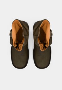 Bottines en cuir marron avec doublure orange, bout arrondi et coutures. Elles présentent une boucle en métal argenté sur le côté extérieur.