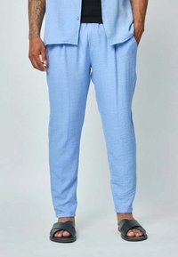 Pantalons lâches de couleur bleu clair, en tissu texturé, avec une taille élastique et des jambes fuselées, associés à des sandales noires.