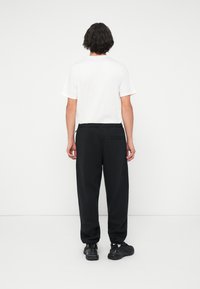 Sorte, løstsiddende joggingbukser med elastisk talje og en enkelt baglomme, parret med en enkel hvid t-shirt med korte ærmer og sorte sneakers.