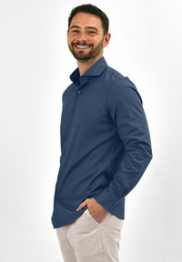 Marineblauwe overhemdblouse met lange mouwen en een klassieke kraag. De stof lijkt glad; heeft zes knopen aan de voorkant.