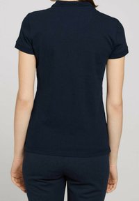 Mörkblå kortärmad pikétröja med ribbad krage, slät textur och en figurnära design, visas från baksidan med lätta sömdetaljer.