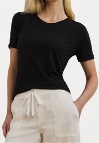 Svart, kortärmad t-shirt med rund halsringning, mjuk textur och slimmad design, kombinerad med krämfärgade linneshorts med dragsko.