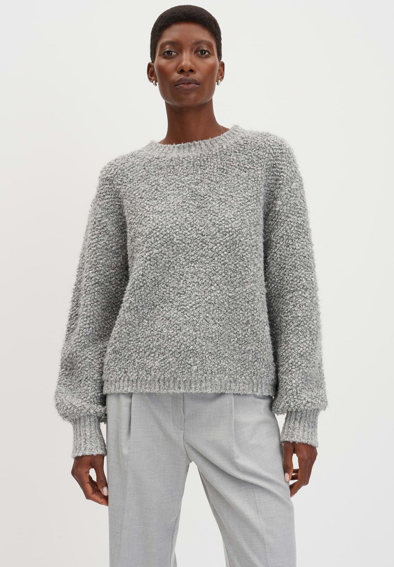 Maglione grigio con texture, colletto tondo e maniche lunghe. Il maglione presenta polsini e orlo a coste, abbinato a pantaloni grigi chiari.