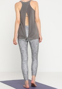Top sin espalda de color gris con detalle retorcido, combinado con leggings ajustados que presentan un patrón de leopardo en blanco y negro.