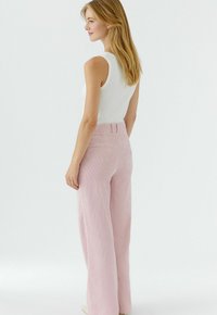 Pantalon large en velours côtelé rose avec des rayures verticales, taille haute et poches arrière, assorti à un haut blanc sans manches. Texture lisse.
