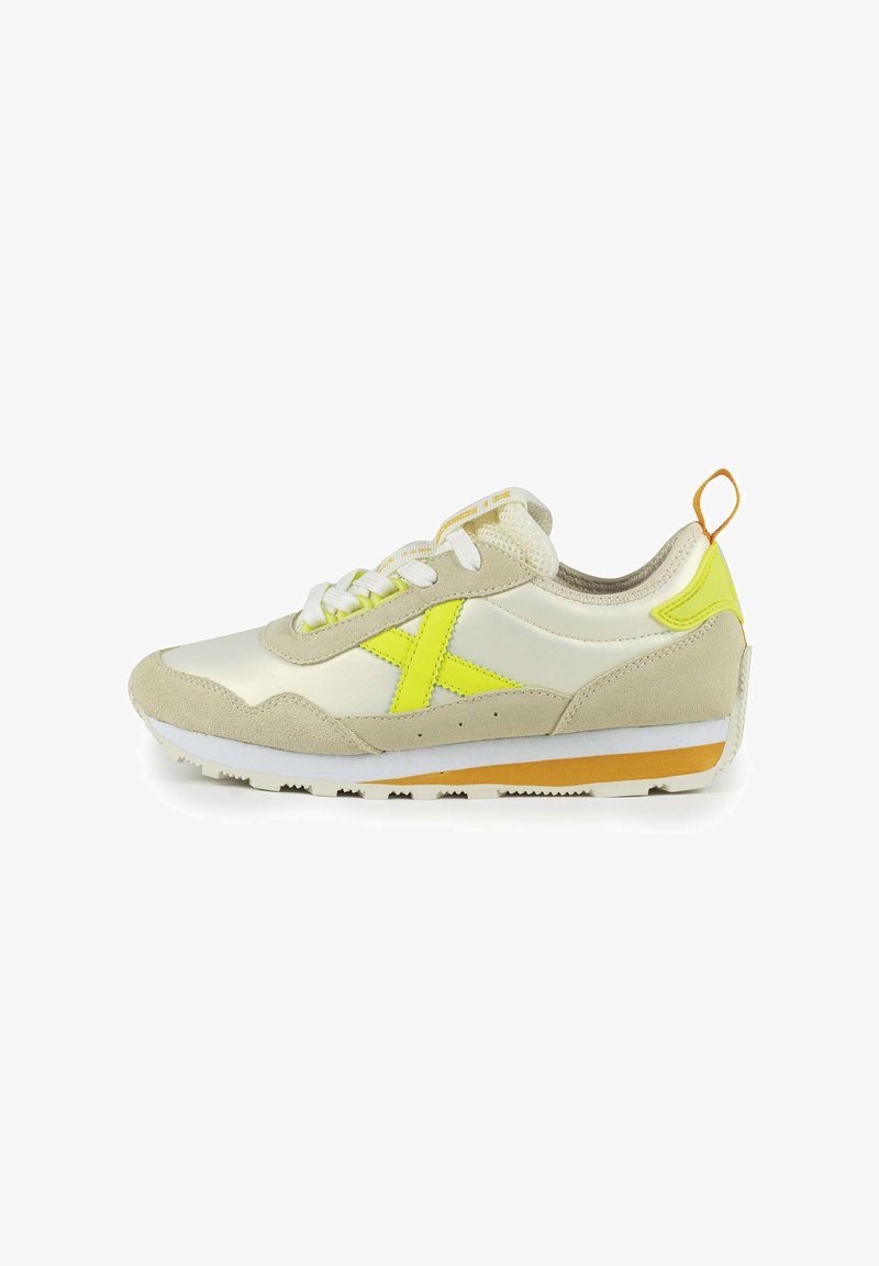Sneaker with a light beige suede and shiny material. Features a bright yellow accent and logo, white laces, and a tan rubber sole.