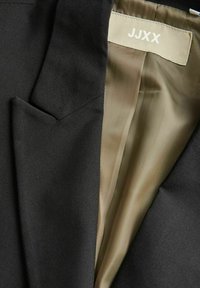 Black blazer with a sleek design, featuring a textured exterior and smooth beige lining. The label reads "JJXX." Includes a chest pocket.