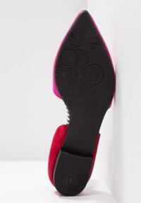 Chaussure à talons hauts avec une tige en daim rose vif et une semelle en caoutchouc noire. La semelle présente des motifs embossés et des détails de marque.