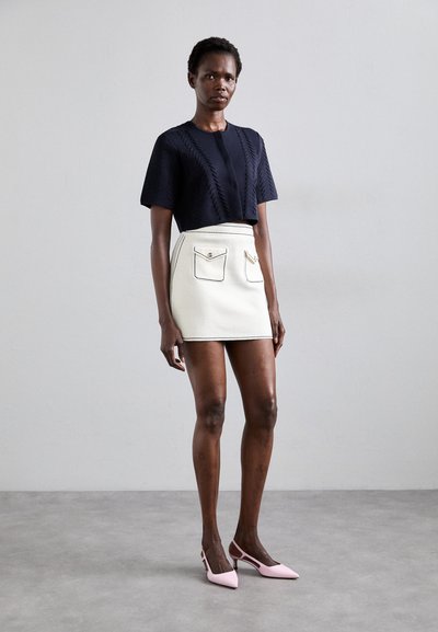 Marineblå strikket top med kortærmer og struktureret design, parret med en hvid mini-skjørt med to lommer og sort syning, suppleret med rosa slingback hæle.