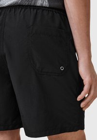 Pantaloni corti neri realizzati in materiale leggero. Presentano una vita elastica, una tasca posteriore con un design esagonale e un dettaglio in grommet metallico.