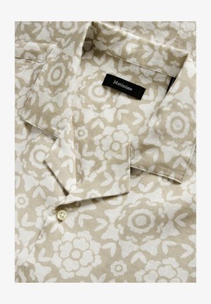 Cămașă din in cu mânecă scurtă în bej, cu un model floral alb, având o închidere cu nasturi și un eticheta neagră pe care scrie "Matinique."