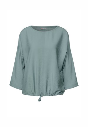 Lichtblauwe blouse met driekwart mouwen, ronde halslijn en een geraffineerde onderrand met een strik; heeft een textuurstof voor extra detail.