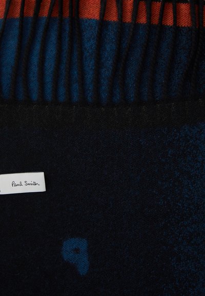 Vilnonis šalikas su tamsiai mėlynomis ir oranžinėmis juostomis, su pūkais. Prisiūta etikete, kurioje rašoma „Paul Smith“. Minkšta tekstūra su subtiliais raštais.
