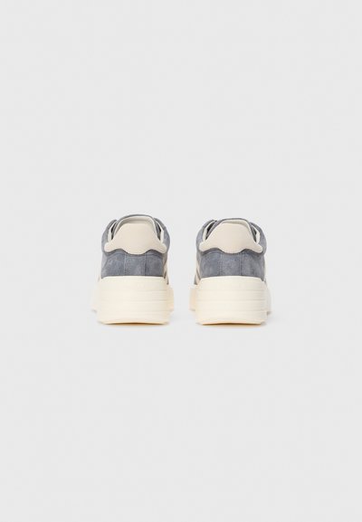 Grijze suède sneakers met een beige hielkraag en dikke off-white rubberen zool, van achteren getoond op een effen witte achtergrond.