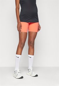 Oransje kompresjons-shorts, svart tettsittende topp, hvite ribbestrikkede sokker med svart Nike-logo, og hvite treningssko med svarte detaljer.