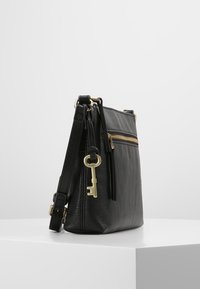 Black leather crossbody bag with a textured finish, featuring a gold zipper and key charm accent. Compact design with an adjustable strap.