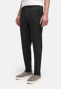 Sorte skreddersydde bukser med en glatt tekstur, med rett ben-design og diskrete frontfold, sammen med grå semsket skinnsko.